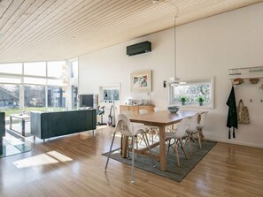 A modern kitchen with a wooden dining table, white chairs, and a large window providing a view of the outdoors. - 4 Star Holiday Home in Vestervig (Vestervig)