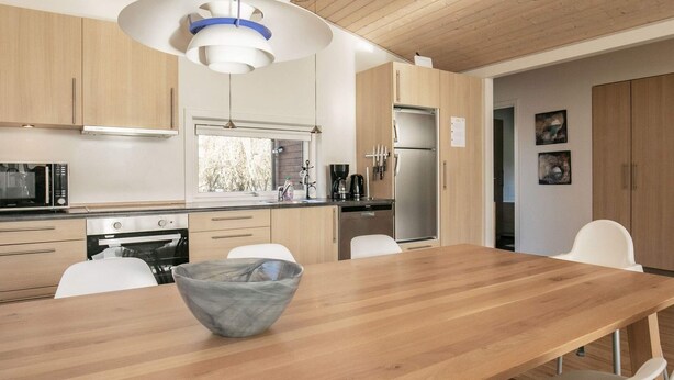 A modern kitchen with wooden cabinets, a stainless steel refrigerator, and a dining area with a wooden table and white chairs.