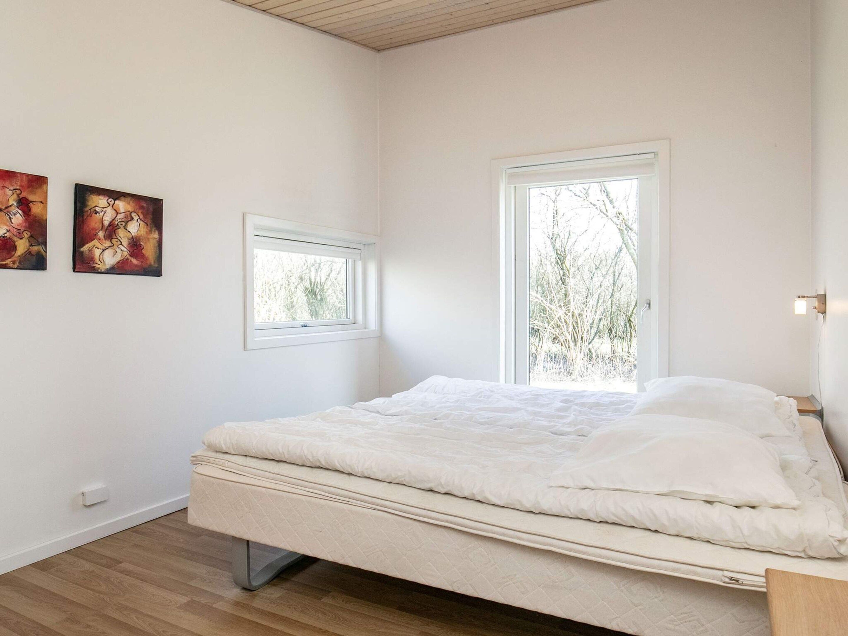A bedroom with a bed, two windows, and two paintings on the wall.