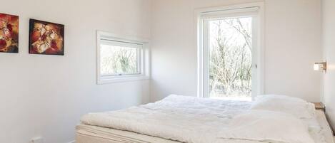 A bedroom with a bed, two windows, and two paintings on the wall.