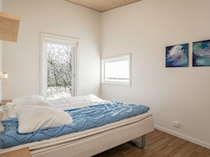 A bedroom with a bed, two windows, and two wall-mounted paintings.
