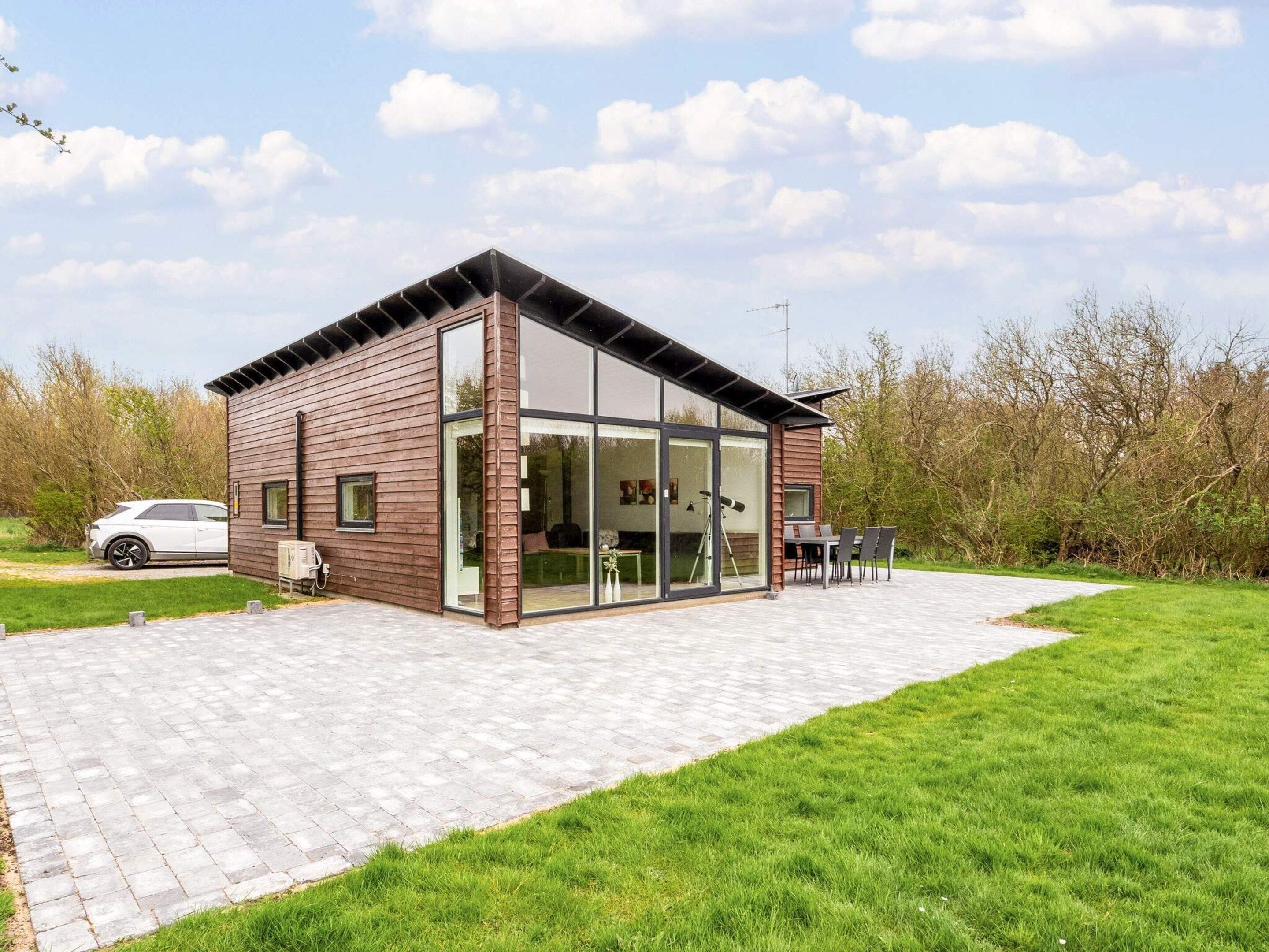 Een modern huis met een grote glazen deur, een terras met tuinmeubilair, en een auto die er geparkeerd staat.