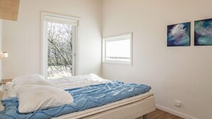 A bedroom with a bed, two windows, and two abstract paintings on the wall.