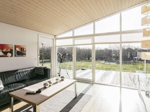 A modern living room with a large window, a black leather sofa, a wooden coffee table, and a telescope. - 4 Star Holiday Home in Vestervig (Vestervig)