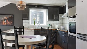 A modern kitchen with a dining area, featuring a white table, dark chairs, and a window with a view of a cityscape. - 5 Person Holiday Home in Stromstad (Stromstad)