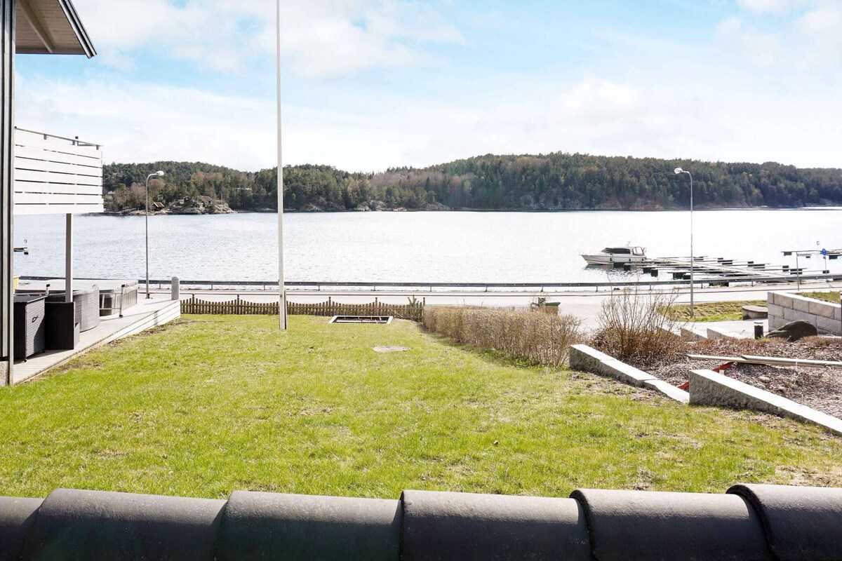 Uma área gramada com vista para um lago e barcos, uma cerca de metal e um edifício com telhado inclinado.