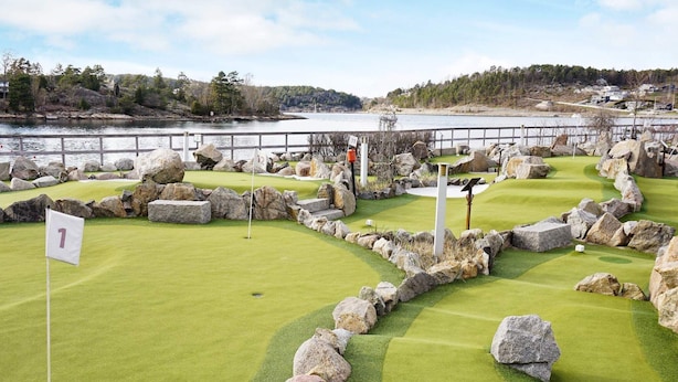 A golf course with a flag marked '1' on the first hole, surrounded by rocks and a water body in the background. - 5 Person Holiday Home in Stromstad (Stromstad)
