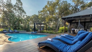 Ein Poolbereich mit Liegestühlen, einer überdachten Sitzecke und einer Pergola.