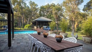 Eine Außenpatio mit Holztisch und weißen Stühlen, umgeben von Topfpflanzen und einem Pool.
