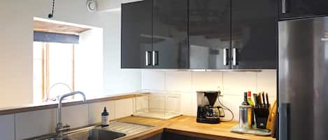 A modern kitchen with black cabinets, stainless steel appliances, and a wooden countertop.