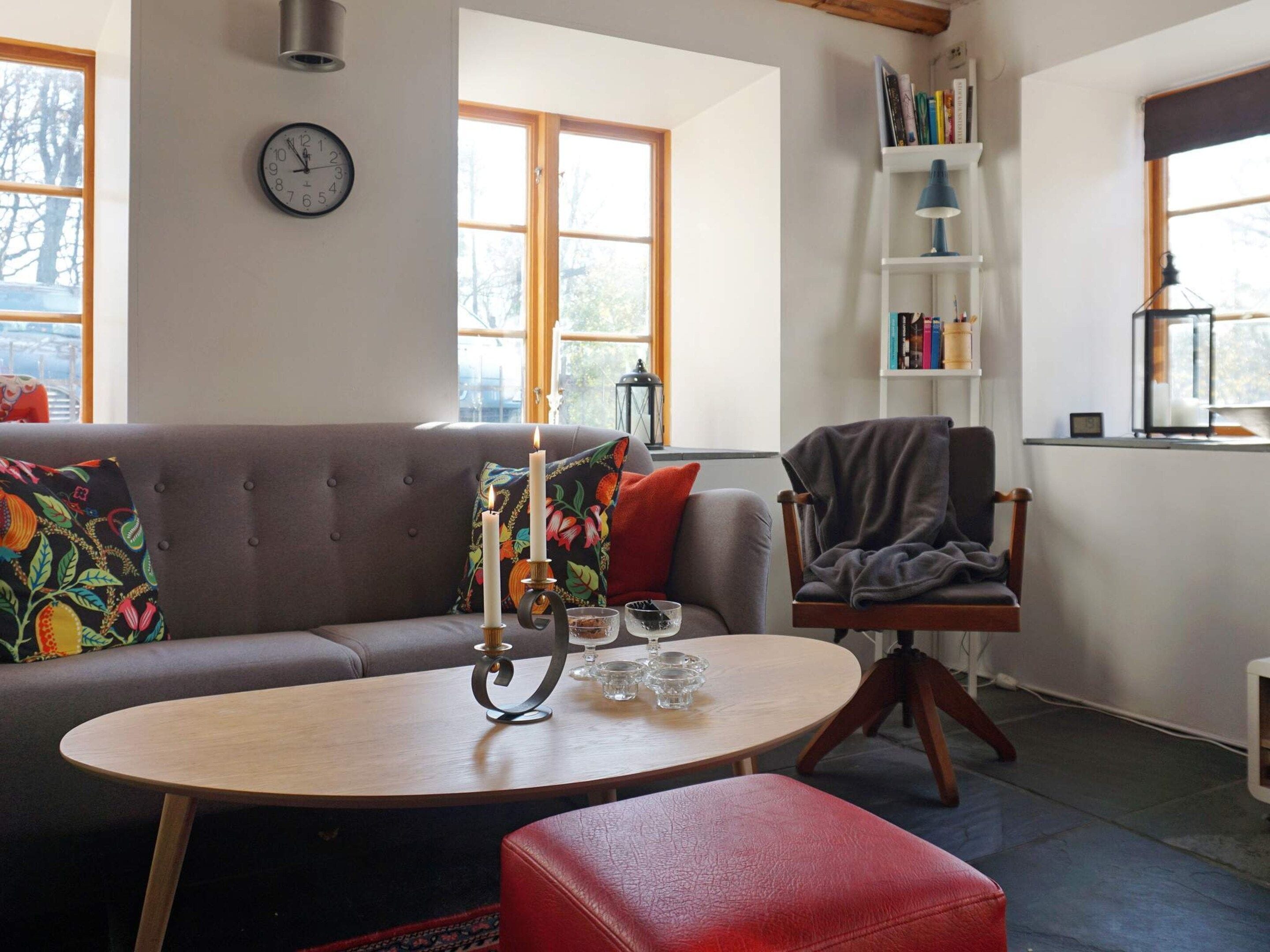 A cozy living room with a sofa, a round table with candles, a bookshelf, and a clock on the wall.
