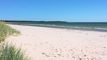 A beach with clear skies, a sandy shore, and a distant landmass.