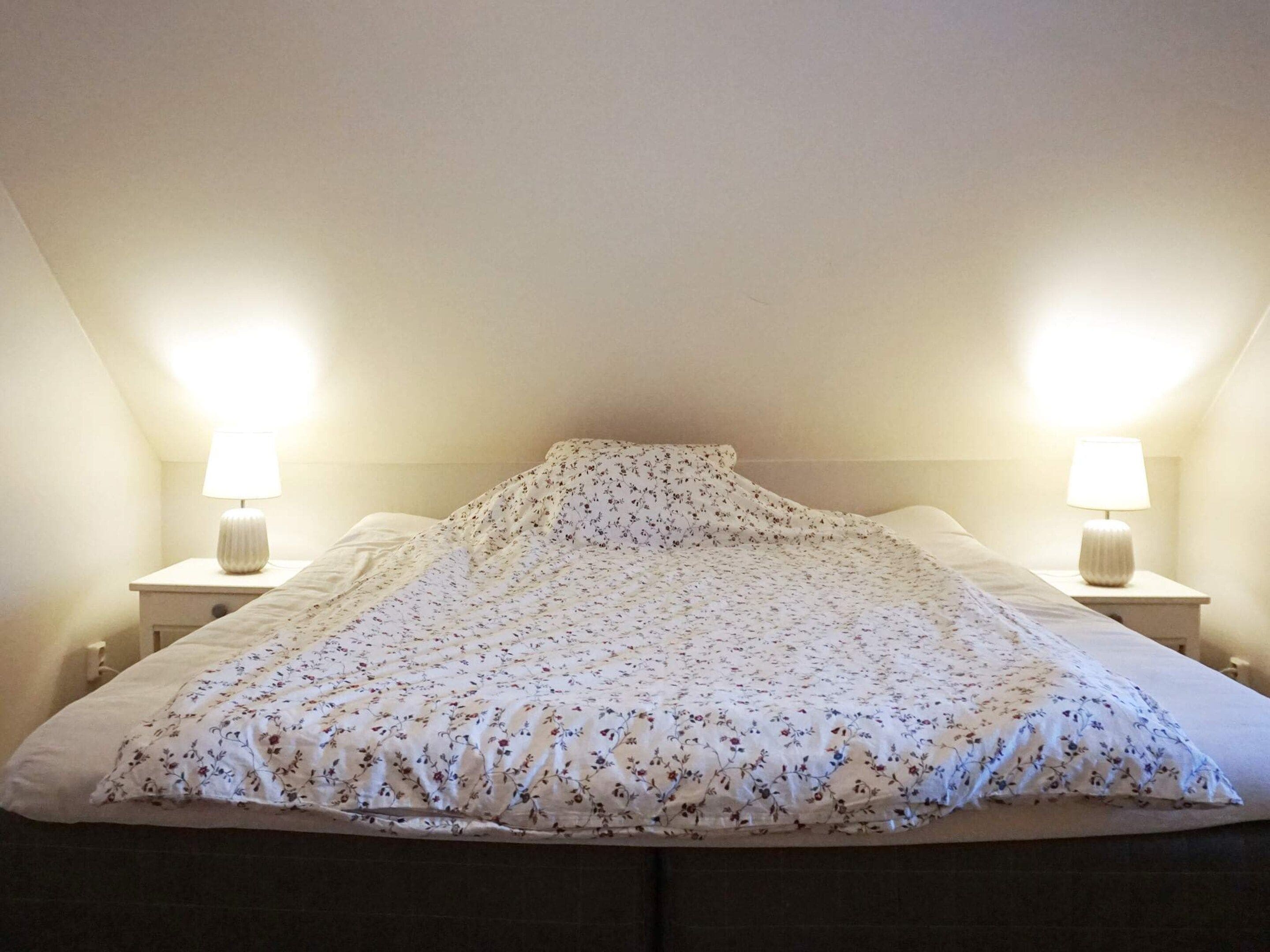 Een slaapkamer met een bed, twee bedlampen en een schuine plafond.
