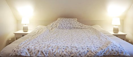 A bedroom with a bed, two bedside lamps, and a sloped ceiling.