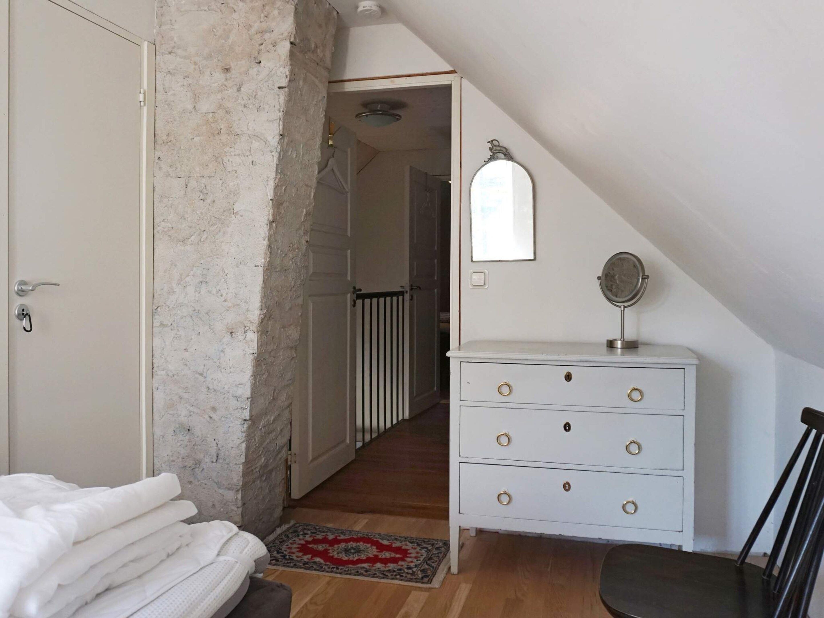 A bedroom with a white dresser, a mirror, a door, and a staircase leading to another room.