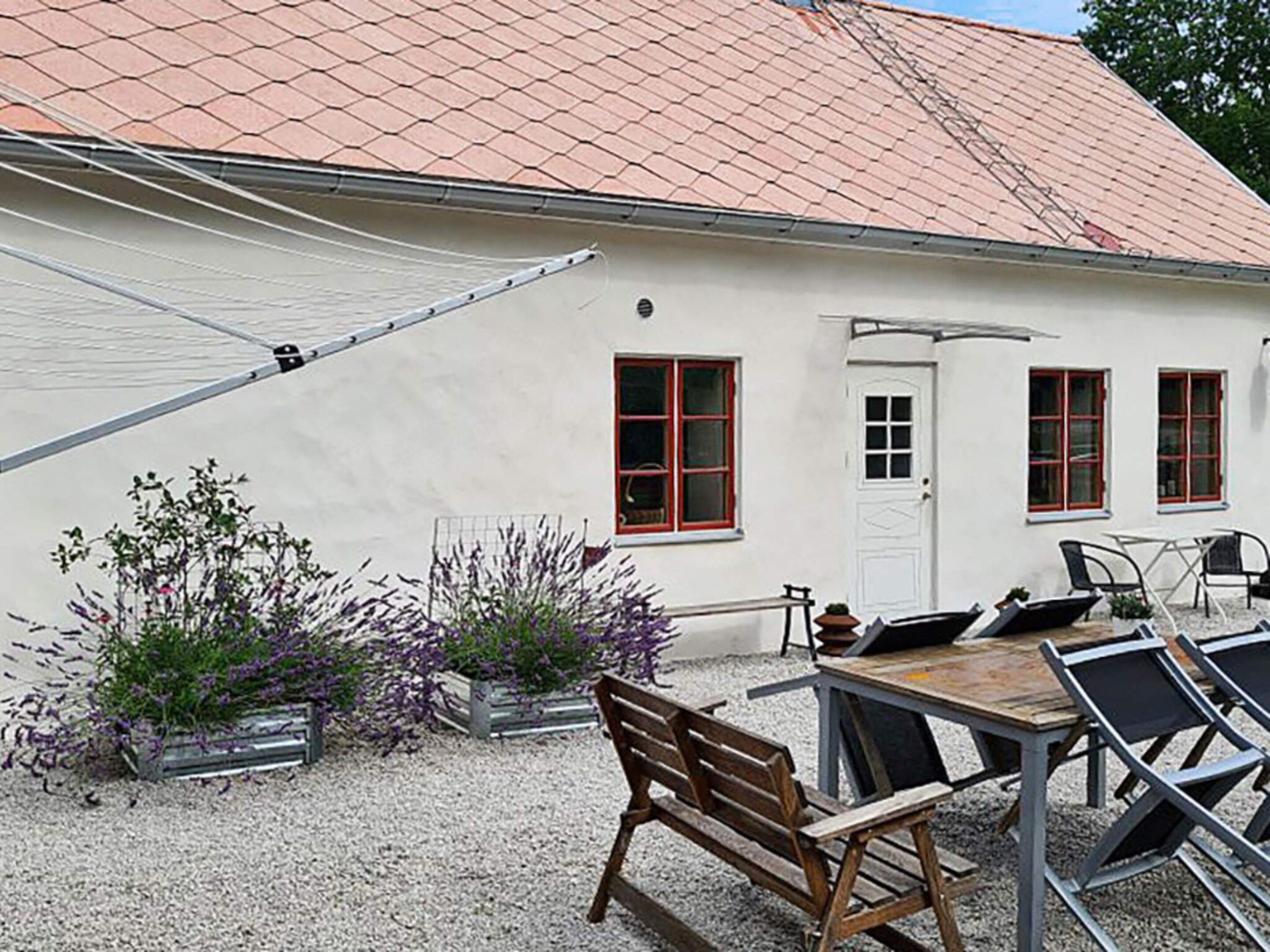 A building with a white exterior, red-framed windows, a door, and a table with chairs.