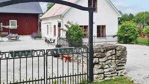 A white building with a stone wall, a red barn, and a fenced outdoor area with tables and chairs. - 4 Star Holiday Home in Slite (Slite)