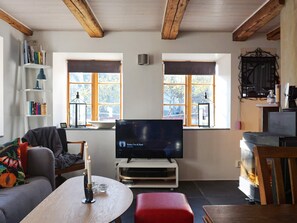 A cozy living room with a television, bookshelves, a red ottoman, and wooden beams on the ceiling. - 4 Star Holiday Home in Slite (Slite)