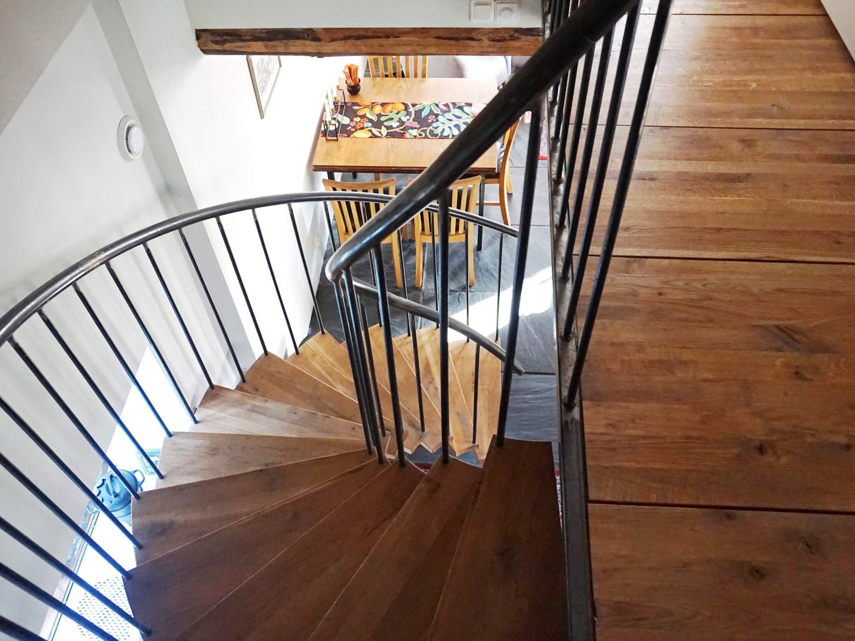 A wooden spiral staircase with metal railings leading to a dining area with a table and chairs.