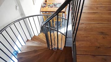 A wooden spiral staircase with metal railings leading to a dining area with a table and chairs.