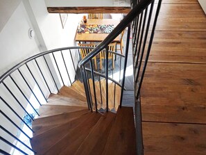 Una scala a chiocciola in legno con ringhiere in metallo che conduce a una sala da pranzo con tavolo e sedie.