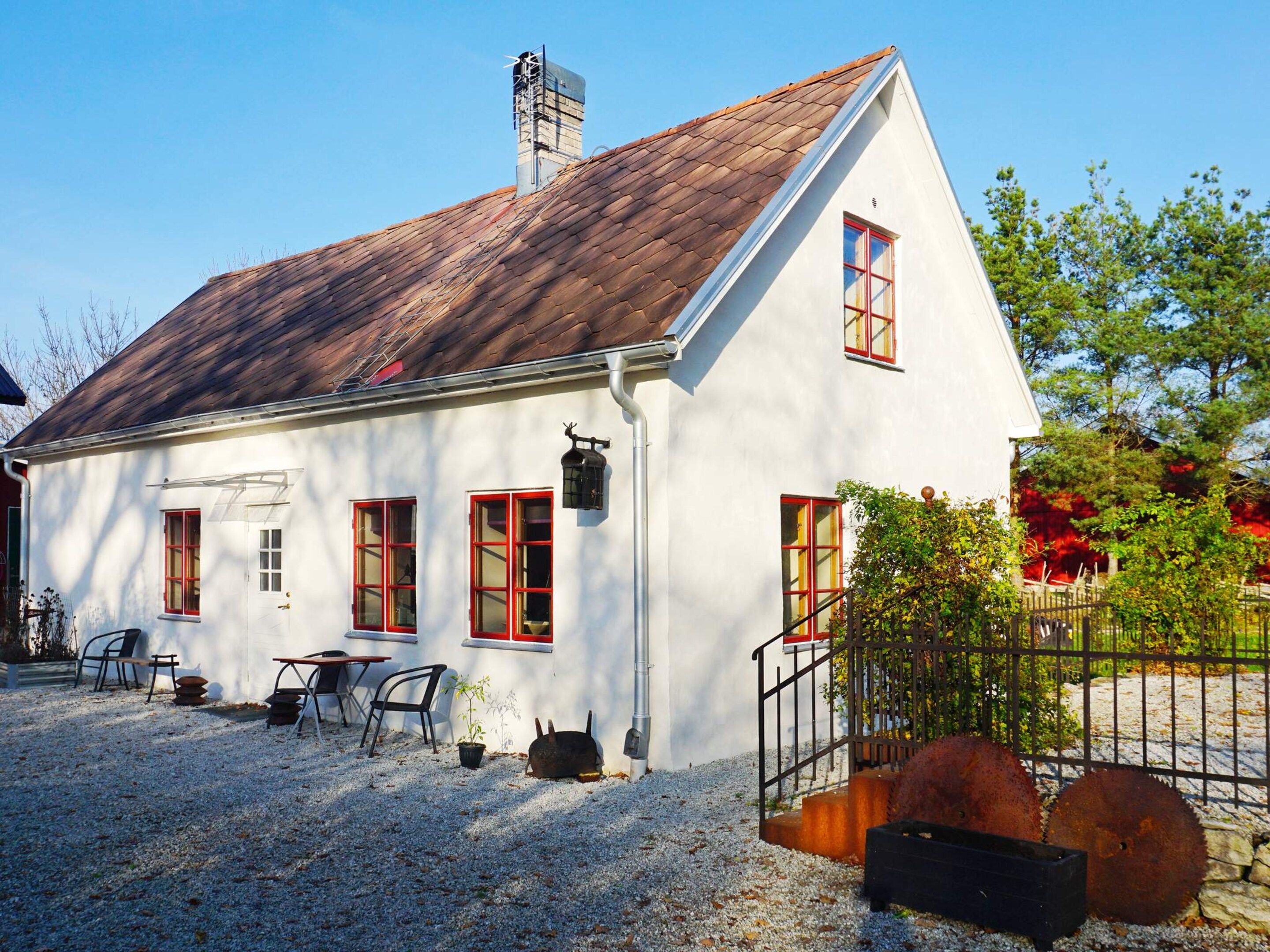 A white building with red-framed windows, a sloped roof, and a gravel driveway.