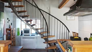 A kitchen with a wooden staircase, a white refrigerator, and a microwave on the counter.