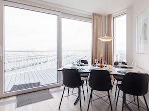 A dining area with a table set for four, large windows, and a view of the water.