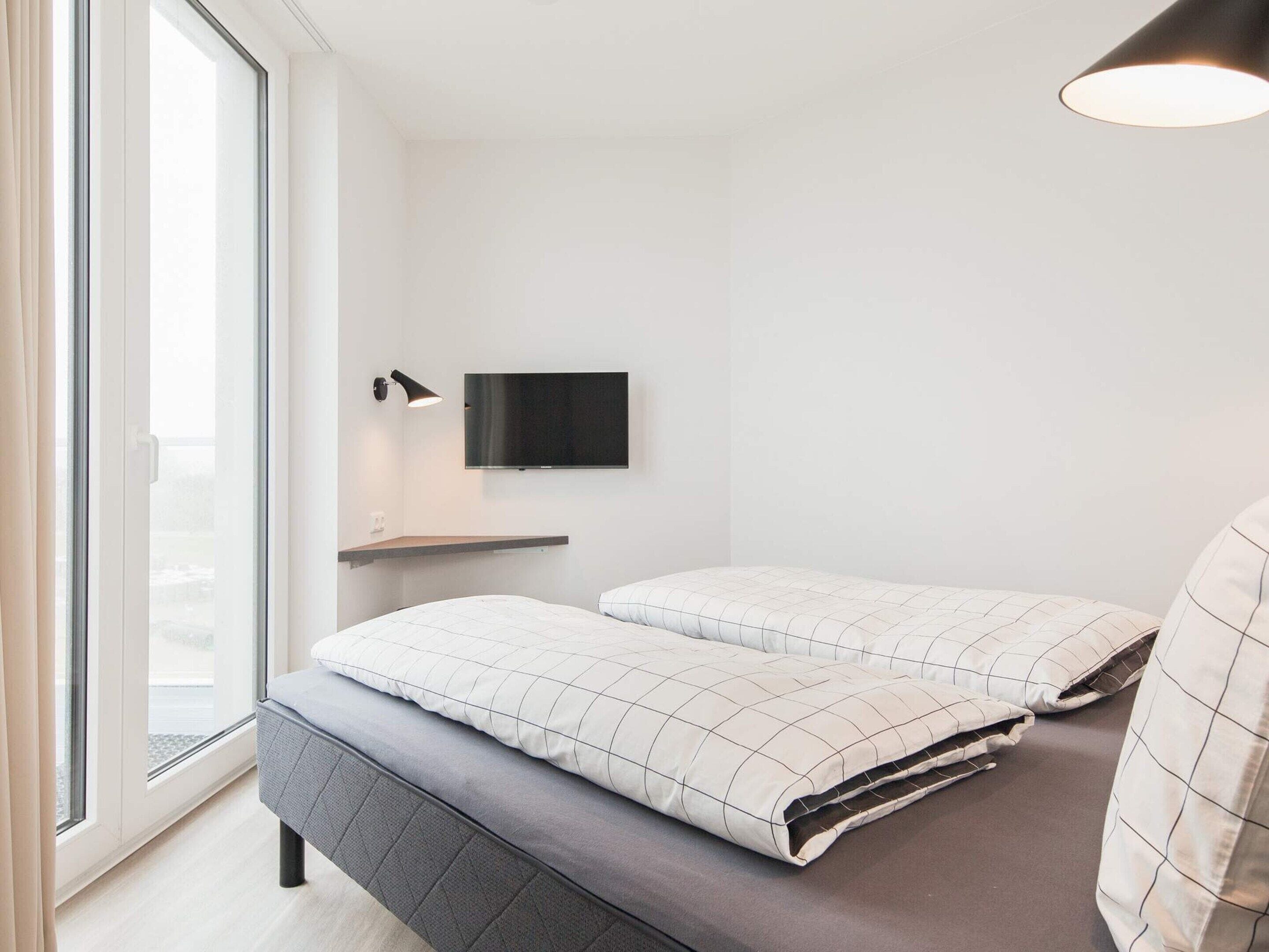 Een moderne slaapkamer met een bed, een tv aan de muur en een raam.