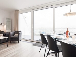 Uma sala de jantar moderna com mesa posta para quatro pessoas, um sofá e uma janela grande com vista.