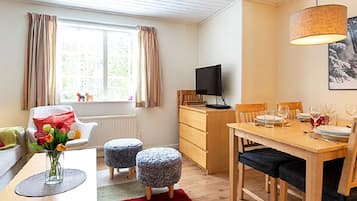 Una habitación acogedora con una mesa de comedor para dos personas, un televisor sobre un escritorio de madera y una ventana con cortinas.