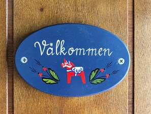 Un letrero azul en forma de óvalo con el texto 'Välkommen' y un adorno de caballo rojo.
