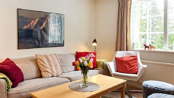 Una sala de estar con sofá, sillón, mesa de centro y un cuadro en la pared.