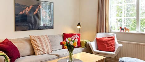 Una sala de estar con sofá, sillón, mesa de centro y un cuadro en la pared.