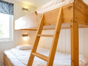 Una cama litera con escalera de madera, ropa de cama blanca y una ventana con cortina.