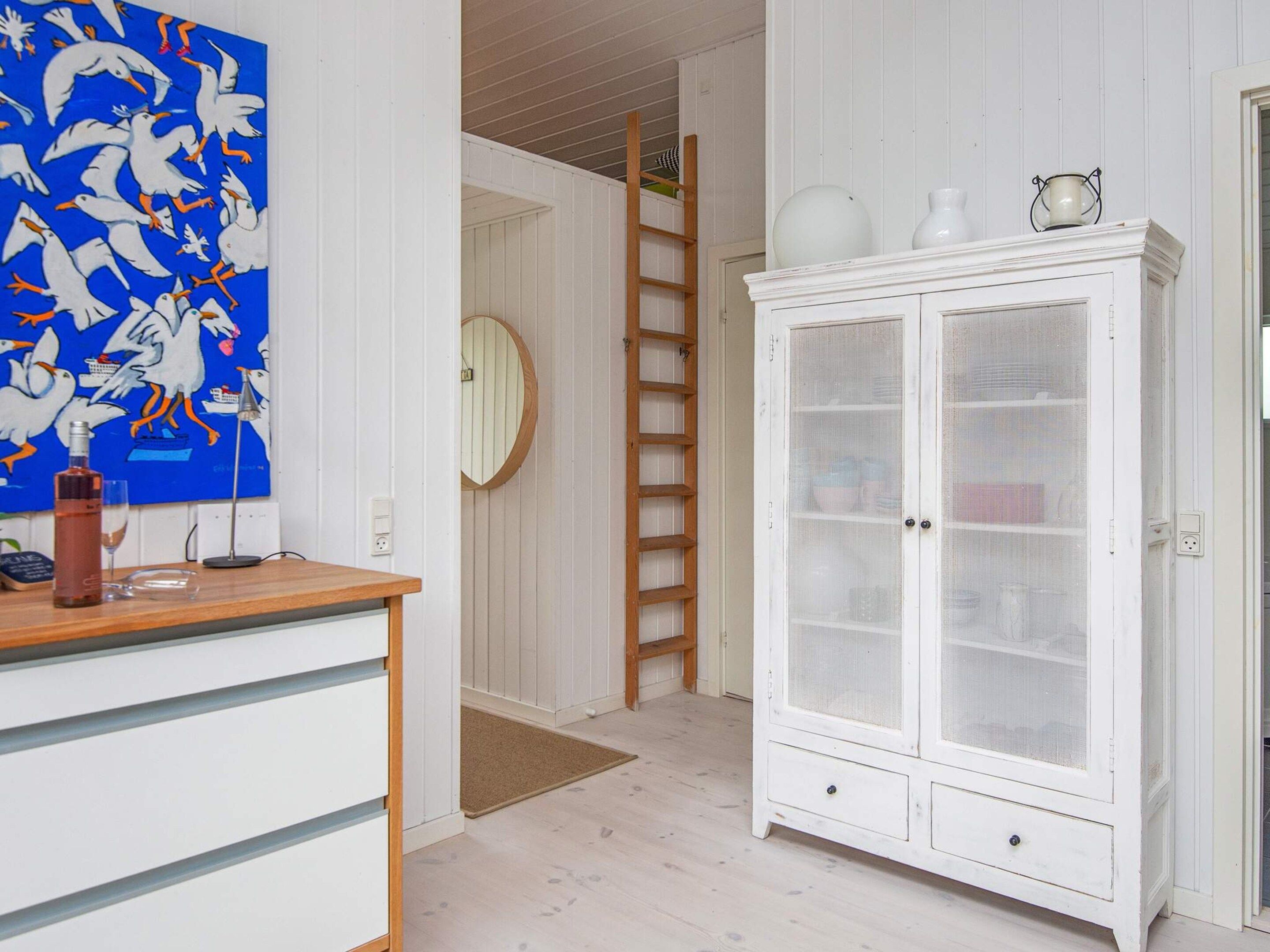 Quarto com escrivaninha de madeira, armário branco com portas de vidro, pintura azul e escada de madeira.