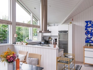 A modern kitchen with a stainless steel refrigerator, white cabinetry, and a large window providing a view of greenery outside. - 4 Star Holiday Home in Malling (Malling)