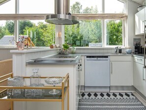 A modern kitchen with a dishwasher, a window overlooking greenery, and a glass display case with crystal glasses. - 4 Star Holiday Home in Malling (Malling)