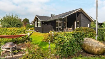 A modern house with a dark exterior, a well-maintained garden, and a large rock feature.