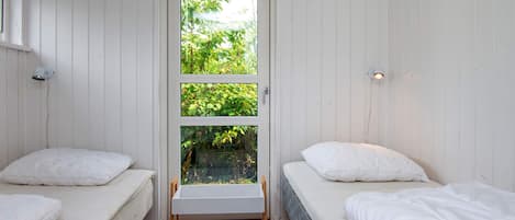 A room with two beds, a window with a view of greenery, and a door.