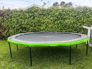 A trampoline with a green safety border, set on a grassy lawn with a hedge in the background.