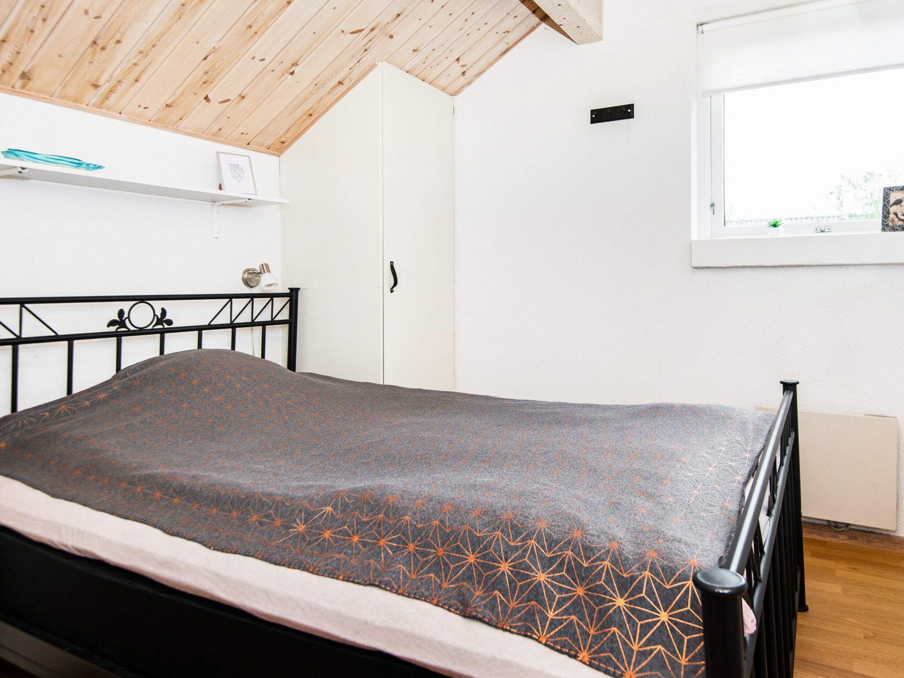A bedroom with a bed, a wooden ceiling, a white wardrobe, and a window with a view.
