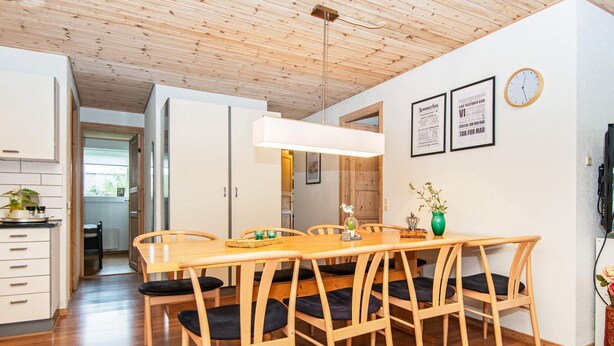 A dining area with a wooden table and chairs, a hanging light fixture, and a clock on the wall. - 4 Star Holiday Home in Juelsminde (Horsens)