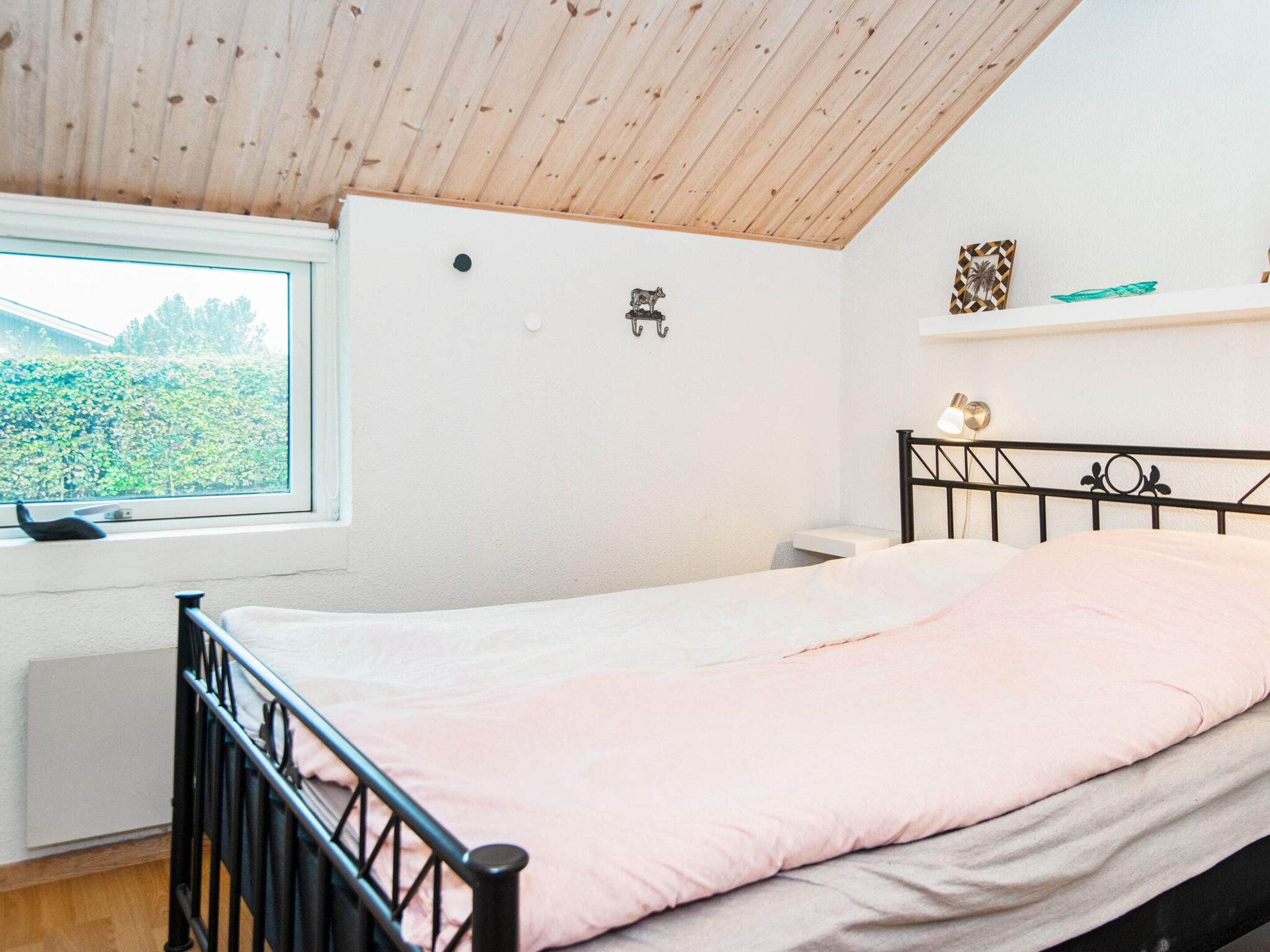 Un dormitorio con cama, ventana, radiador y estante fijado a la pared.