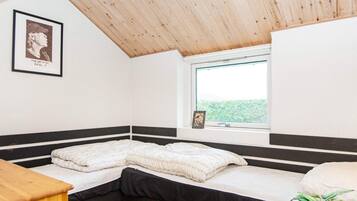 Een slaapkamer met een houten plafond, een raam met uitzicht, een bed met een zwart hoofdeinde en een lijst met een foto aan de muur.