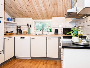 A modern kitchen with white cabinets, a wooden ceiling, and a window with a view of greenery. - 4 Star Holiday Home in Juelsminde (Horsens)