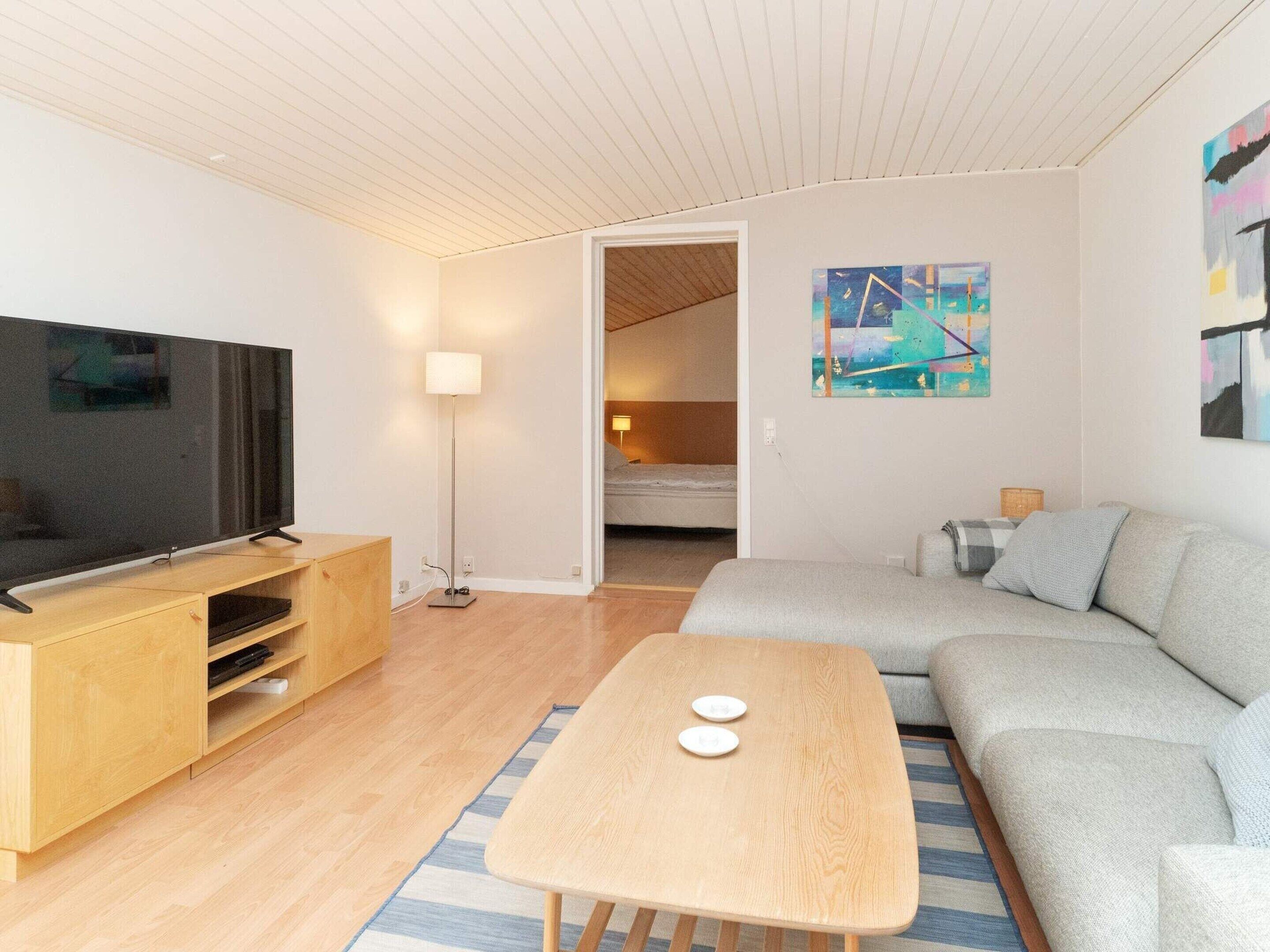 A modern living room with a flat-screen TV, a wooden coffee table, a grey sofa, and a painting on the wall.