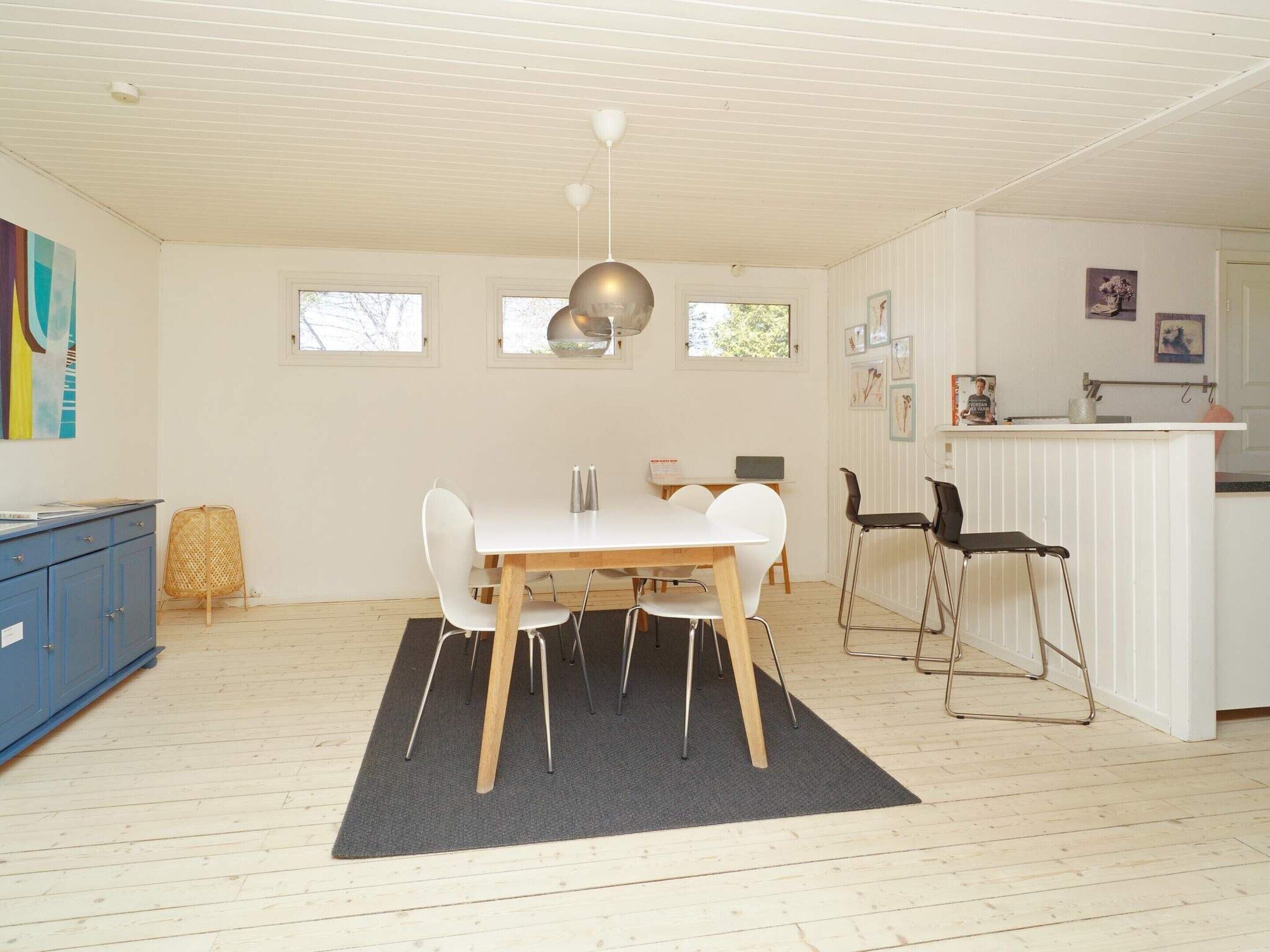 A dining area with a white table, chairs, and a black rug. There is a blue cabinet and a wicker chair in the corner.