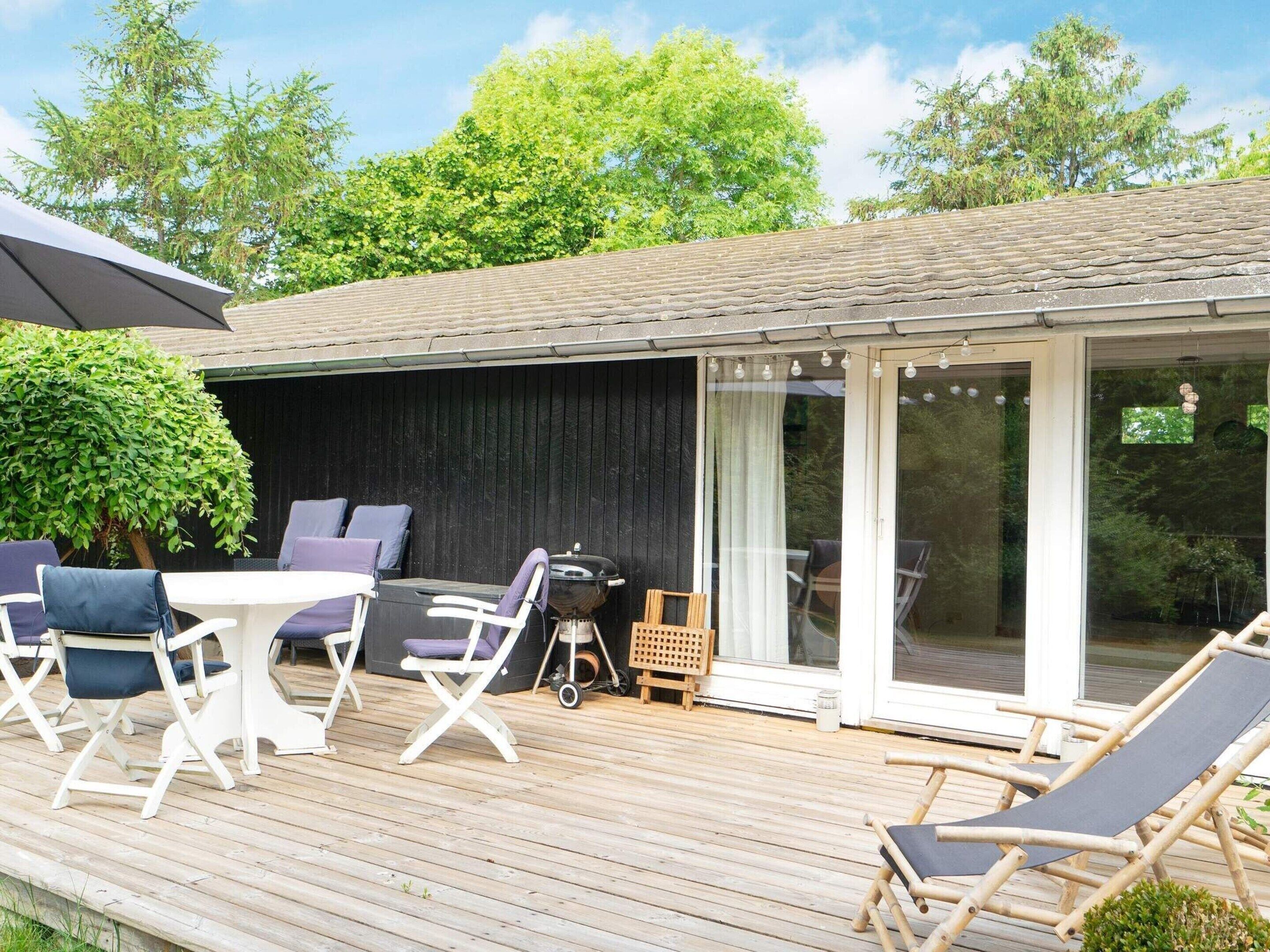 A wooden deck with outdoor furniture, a grill, and a glass-enclosed patio area.