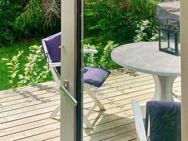 An outdoor deck with a round table and two chairs, surrounded by lush greenery. - 4 Person Holiday Home in Graested (Graested)